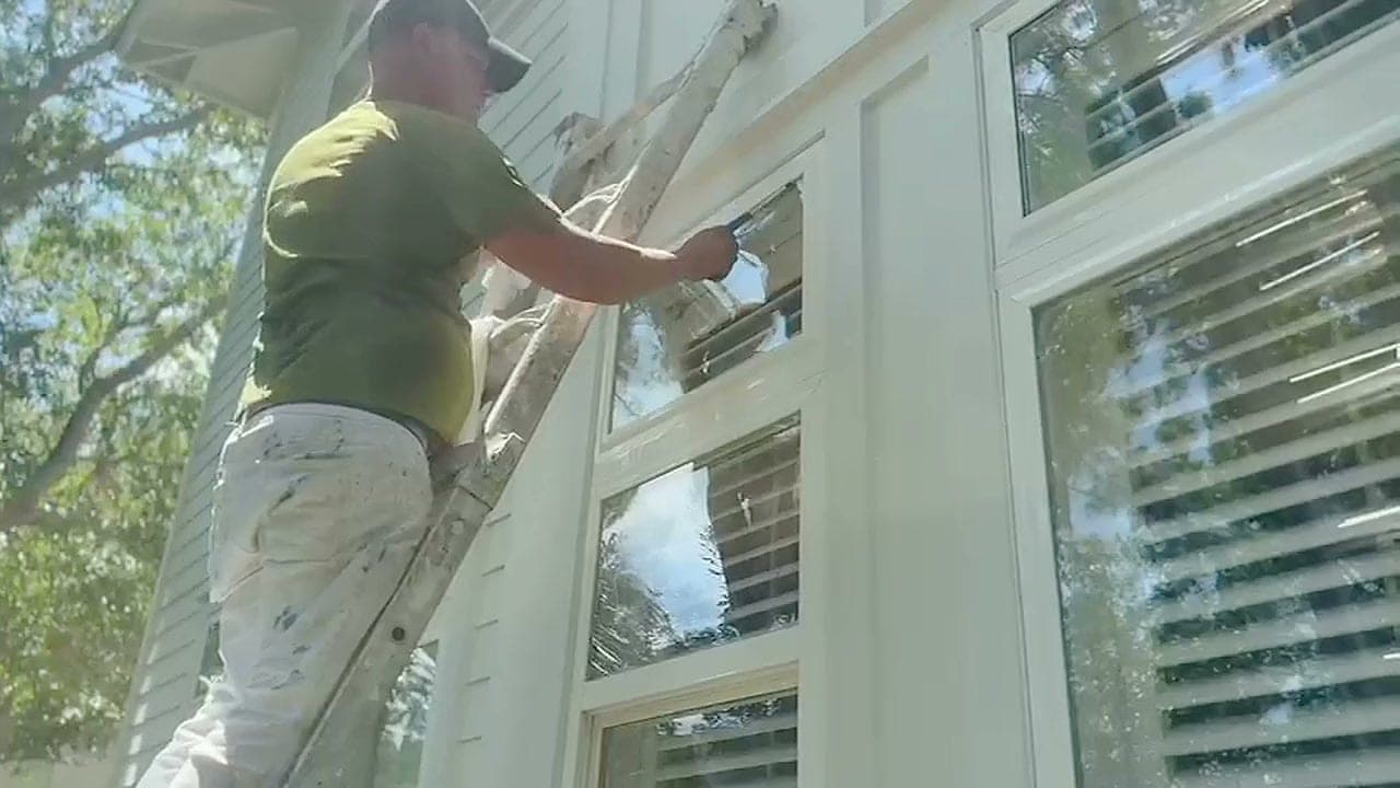 Cucol LLC painter on a ladder working on a white two-storey home