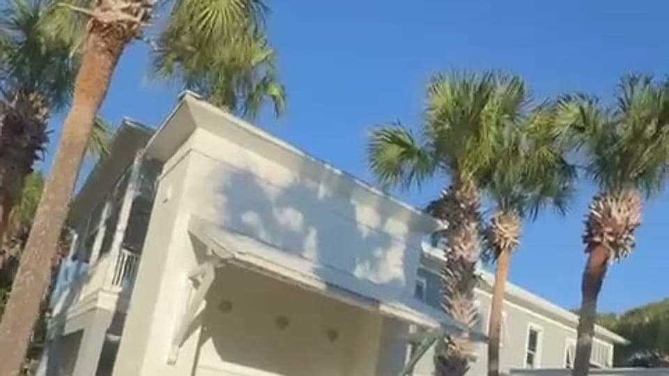 White beach house among palm trees under a blue Florida sky