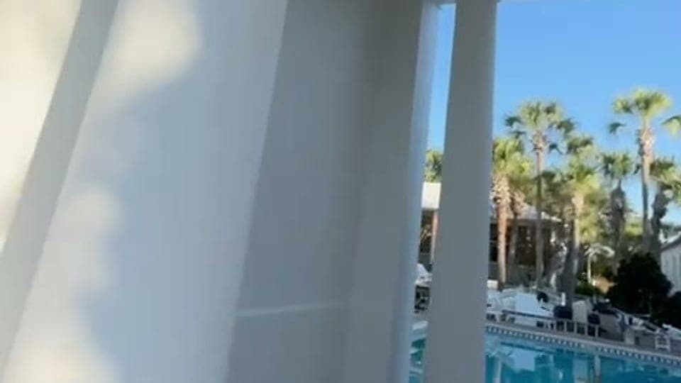 Pool deck and palm trees seen past a white column at a coastal property