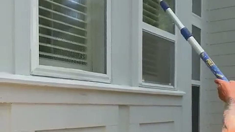 Soft washing white board-and-batten siding with an extension pole